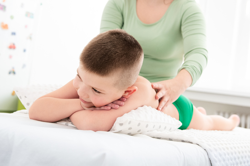 Kids massage concept background. Young female massage therapist giving a 6 year old boy back massage. Physical therapy.